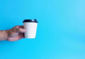 mão de homem segurando uma xícara de café branco, cheia de café preto quente americano, sem açúcar sem leite, pronto para beber, refrescante. aroma acordado fresco para trabalhar colocado em um fundo azul isolado foto