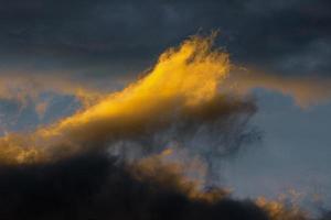 deslumbrante fofo trovoada nuvens iluminado de desaparecendo raios às pôr do sol, Sombrio nuvens de tempestade flutuando através azul céu para mudança estação clima foto