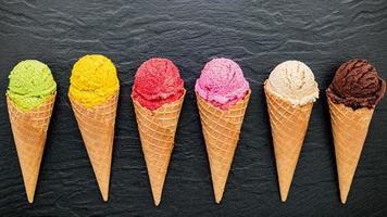 vários sabores de sorvete em cones em fundo de pedra escura foto