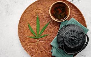 bule vintage com chá de ervas de cannabis e folhas de maconha fresca montado no fundo de concreto foto