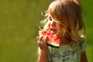 fofa pequeno menina segurando uma peça do Melancia dentro a jardim dentro horário de verão foto