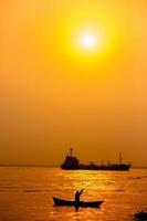 tarde dourado pôr do sol tempo, uma pescador pescaria em a beira-mar em uma barco. foto