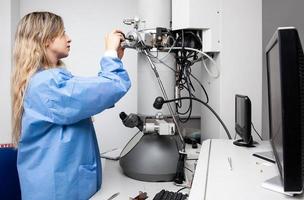 jovem fêmea cientista Carregando uma espécime usando uma amostra suporte para dentro uma transmissão elétron microscópio foto
