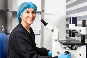 retrato do uma fêmea cientista dentro a laboratório Próximo para a invertido microscópio. foto