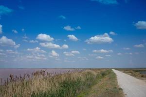 estrada de terra e campos próximos ao lago sasyk-sivash com céu azul nublado na criméia foto