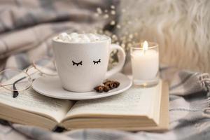 xícara de chocolate quente com marshmallows no livro com vela foto