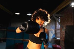 mulheres auto defesa poder. africano americano mulher lutador soco com boxe luvas para Câmera. saudável Forte menina soco Treinamento socos olhando concentrado direto. em forma corpo dar certo. foto