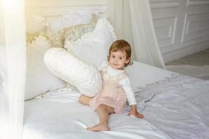 fofa pequeno menina pulando em branco cama foto