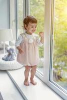 pequeno menina em pé em janela peitoril foto