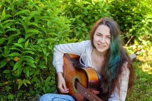 jovem mulher sentado dentro Relva e jogando guitarra foto