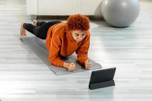 ginástica exercite-se treinamento. jovem saudável em forma africano menina fazendo prancha exercício em ioga esteira em chão às lar. Atlético mulher dentro roupa de esporte Treinamento pilates. esporte e fitness. foto