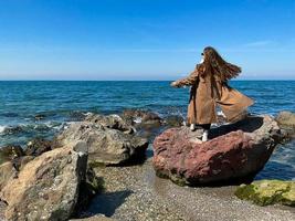 menina com grandes cabelo é em pé em Beira Mar vestido foto