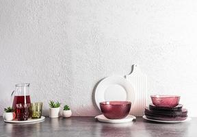 uma conjunto do moderno vidro Borgonha pratos e uma jarro com uva suco em uma pedra bancada dentro a interior do a cozinha. cozinha fundo. foto