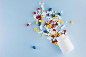 pílulas coloridas caem da garrafa de plástico sobre fundo azul foto