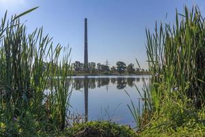 industrial chaminé do térmico poder plantar com reflexão dentro lago foto