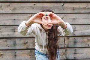 amor, formato de coração, paz. retrato de beleza jovem feliz mulher positiva mostrando sinal de coração com as mãos no fundo da parede de madeira foto