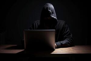 hacker vestindo Preto moletom com capuz usando computador portátil computador enquanto trabalhando em Sombrio fundo. ai gerado foto