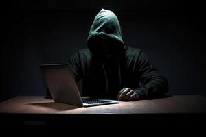 hacker vestindo Preto moletom com capuz usando computador portátil computador enquanto trabalhando em Sombrio fundo. ai gerado foto