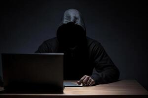 hacker vestindo Preto moletom com capuz usando computador portátil computador enquanto trabalhando em Sombrio fundo. ai gerado foto