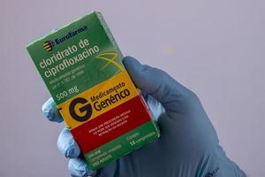 rio, brasil - 27 de janeiro de 2023, mão com luva protetora de borracha segurando caixa de remédios, cloridrato de cipofloxacina foto