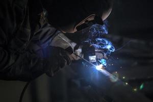 soldador às trabalhar. homem dentro uma protetora mascarar. a soldador faz costuras em a metal. faíscas e fumaça quando Soldagem. foto