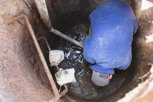 trabalhador limpa a esgoto escotilha.a trabalhador limpa uma esgoto Escotilha. uma homem dentro a Escotilha. foto