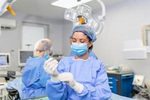 retrato da bela médica cirurgiã calçar luvas médicas em pé na sala de operação. cirurgião na sala de cirurgia moderna foto