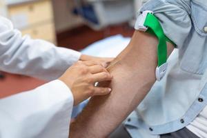 preparação para sangue teste de fêmea médico médico uniforme em a mesa dentro branco brilhante sala. enfermeira pierces a pacientes braço veia com agulha em branco tubo. foto