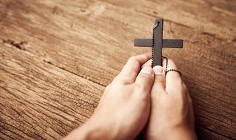 conceito do cristão. fechar acima do mão Rezar segurando uma Jesus Cristo Preto Cruz em a velho de madeira mesa fundo com cópia de espaço foto