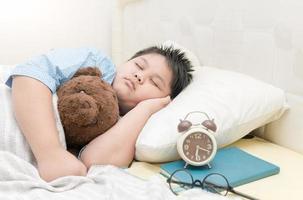 gordo Garoto dormir e abraço Urso de pelúcia Urso em cama foto