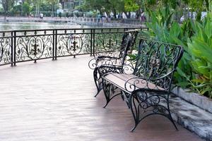 às uma sombrio público parque em uma de madeira terraço de a rio, lá estão dois Banco esperando para pessoas para sentar. Banco fez do forjado ferro com lindo projetos. foto