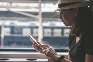 viajante linda jovem usando o smartphone em uma estação de trem, transporte e conceito de estilo de vida de viagens foto