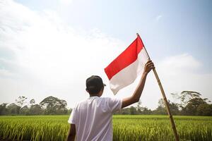 uma homem segurando uma vermelho e branco Indonésia bandeira em topo do uma exuberante verde arroz campo. ai gerado foto