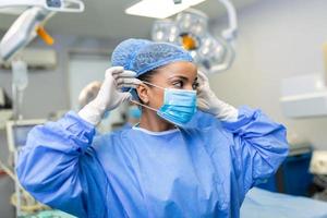 retrato do lindo fêmea médico cirurgião colocando em médico mascarar em pé dentro Operação sala. cirurgião às moderno operativo quarto foto