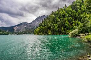 lago verde emoldurado pela floresta e montanhas com céu nublado