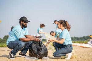 voluntariado, caridade, limpeza, pessoas e ecologia conceito - grupo do feliz voluntários com lixo bolsas limpeza área em arenoso costa. foto