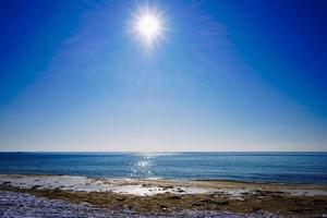 paisagem marinha de uma linha costeira e um corpo de água com sol forte e um céu azul claro foto