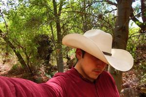 homem dentro uma vermelho camisa e uma branco vaqueiro chapéu é levando uma selfie. foto