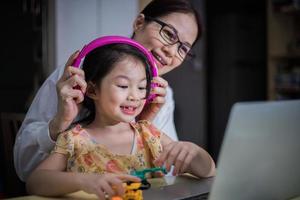 uma mãe está colocando fones de ouvido na filha para ajudá-la a estudar online. foto