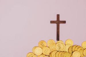 uma cruz é levantada acima de uma pilha de moedas em um fundo rosa pastel foto