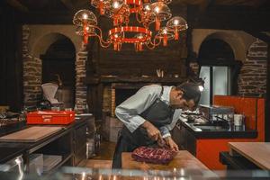 masculino chefe de cozinha corte carne em mesa dentro cozinha às luxo restaurante foto