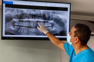masculino meio -envelhecido dentista às dele escritório usando a x raio imagem para explicar tratamento para dele paciente foto