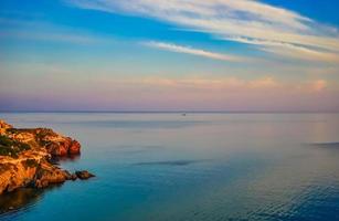 paisagem marinha de uma costa rochosa por um corpo de água com um céu nublado colorido foto