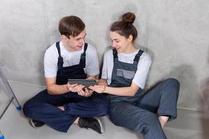 casa faça você mesmo renovação conceito. jovem feliz casal sentado em chão olhando casa reparar plano dentro tábua dentro de casa. mulher mostrando para homem plano interior Projeto on-line. casal dentro Novo casa durante reparar funciona. foto