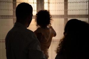 pais e crianças apreciar a manhã luz solar brilhando através a quarto janela dentro a casa. foto