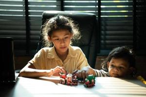 retrato do irmã e pequeno irmão dentro a escritório quarto do casa, elas estão tendo Diversão jogando com brinquedo trens junto. foto