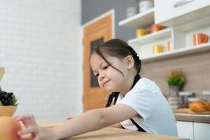 retrato do uma pequeno menina dentro a cozinha do uma casa tendo Diversão jogando com fruta brinquedo e utensílios de cozinha foto