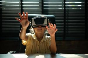 retrato do pequeno menina dentro escritório quarto do casa com gestos este estão expresso quando jogando virtual realidade jogos foto