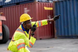 trabalhador homem dentro protetora segurança macacão uniforme com amarelo capacete de segurança e usar walkie talkie Verifica recipiente às carga Remessa armazém. transporte importar, exportar logístico industrial serviço foto