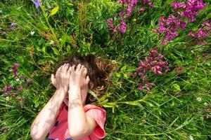 retrato do uma criança menina dentro verão deitado dentro a Relva e flores silvestres com calcanhares e Palmeiras. verão tempo, liberdade foto